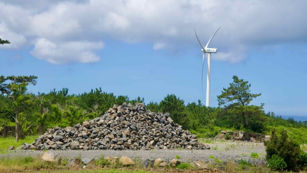 Basalt stone pile with wind turbine behind pines.