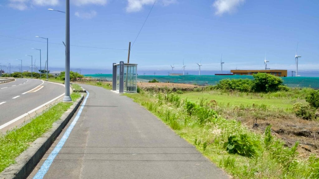 Coastal bus stop and path along Iljuseo Road with turbines offshore.