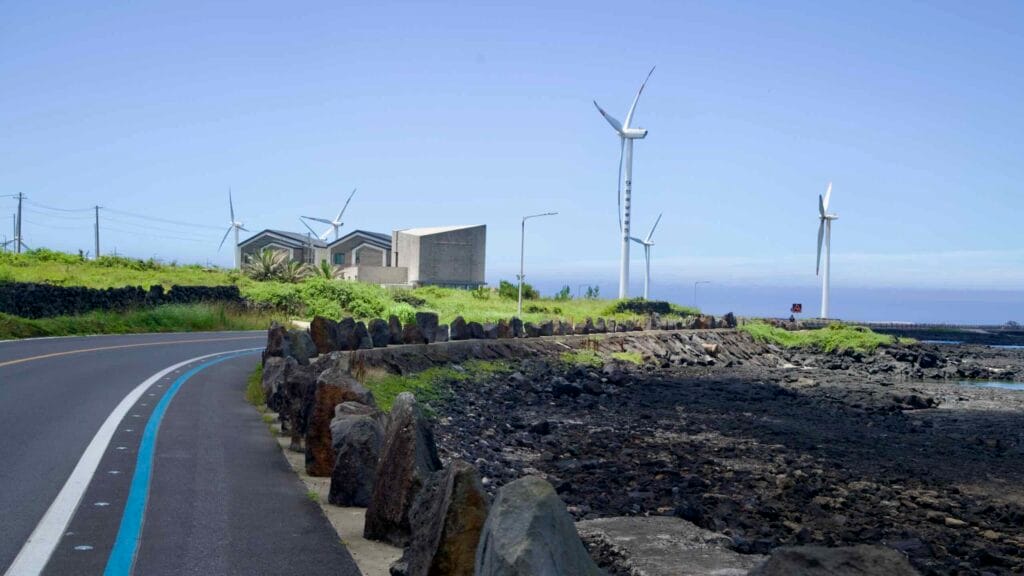 Sinchang Windmill Coastal Road with blue bike line and basalt boulders.