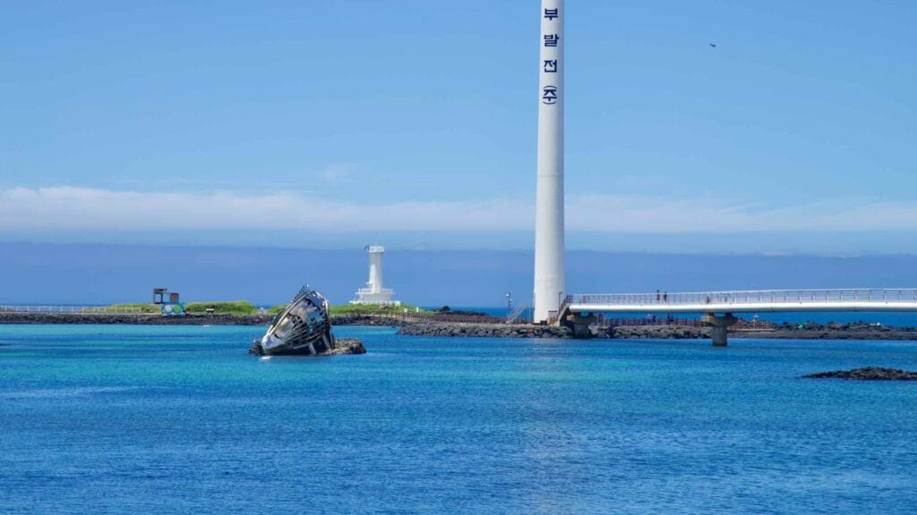 Leaning wrecked boat, white lighthouse, and a turbine at Sinchang’s shore.