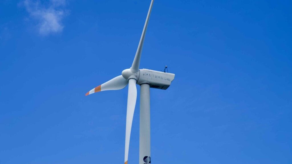 Close view of turbine nacelle and blades against a blue Jeju sky.