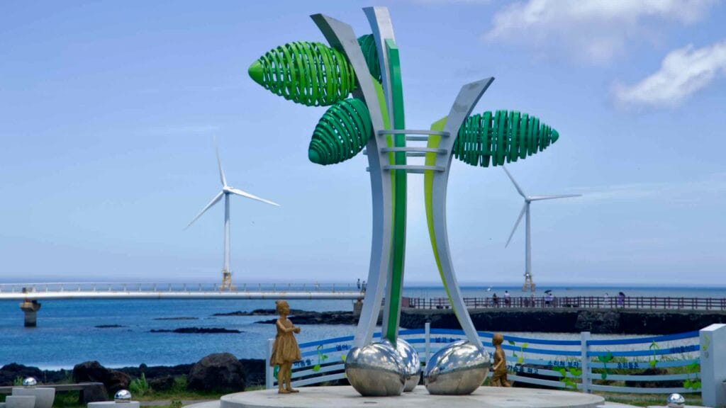 Leaf‑shaped coastal sculpture with children statues and turbines.