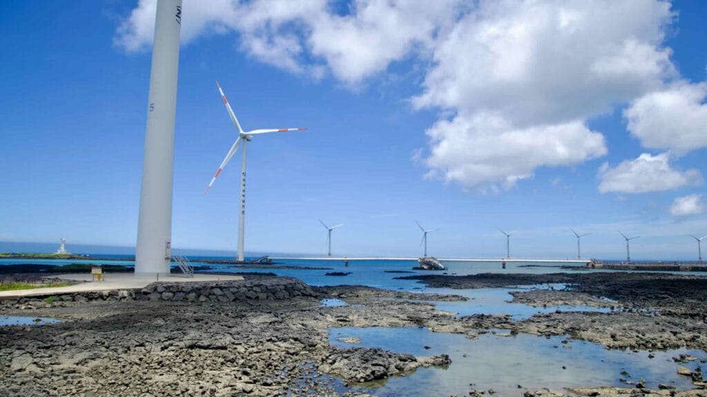 Lava flats and a row of turbines along Sinchang’s coast under clouds.