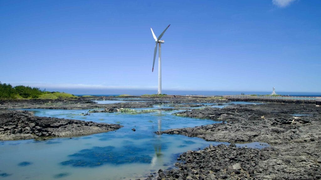 Offshore turbine reflecting in tidal pools with distant lighthouse.