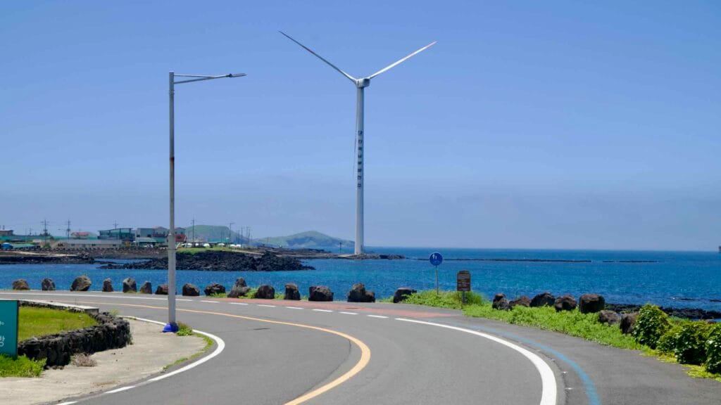 Curving coast road and bike lane leading toward an offshore turbine.