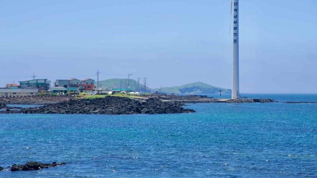 Coastal village opposite a turbine base with green islets beyond.