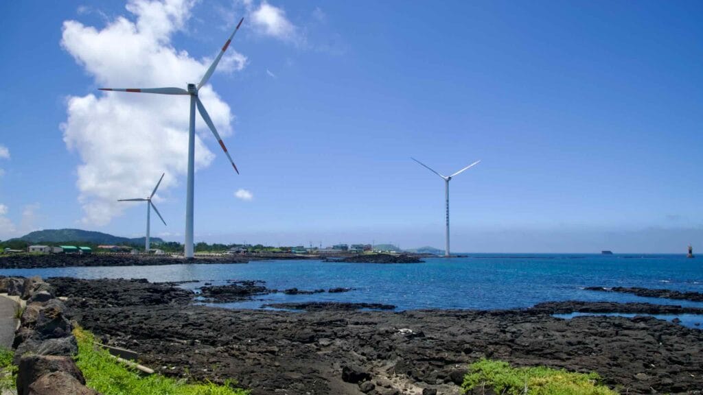 Turbines above basalt inlets along Jeju’s Sinchang coast.