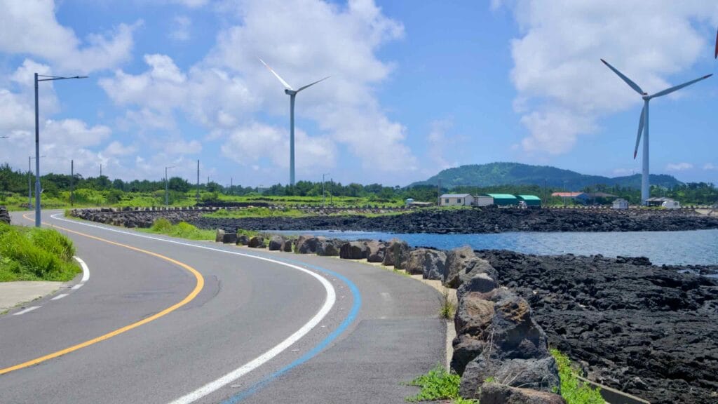 Seaside bike lane sweeps past basalt rocks and wind turbines.