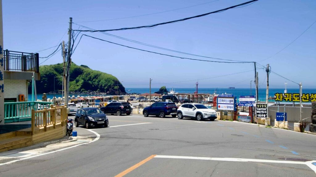 Harbor approach at Chagwido with parking, signs, and the headland beyond.