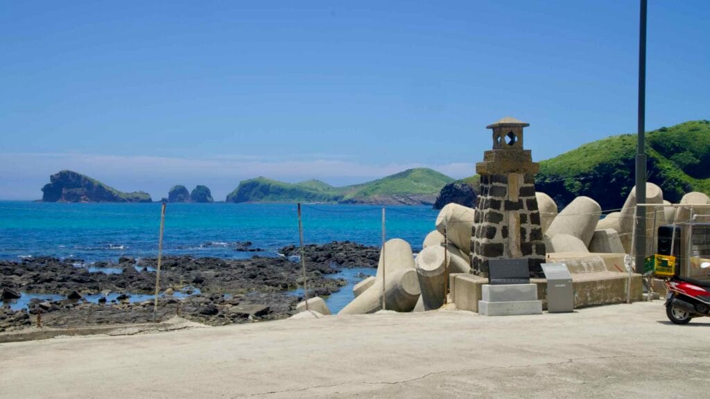 Basalt beacon on the breakwater facing emerald water and offshore islets.