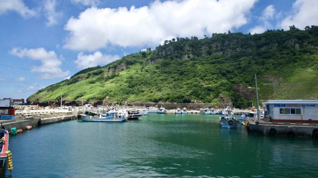 Fishing boats inside calm Chagwido Harbor beneath layered tuff cliffs.