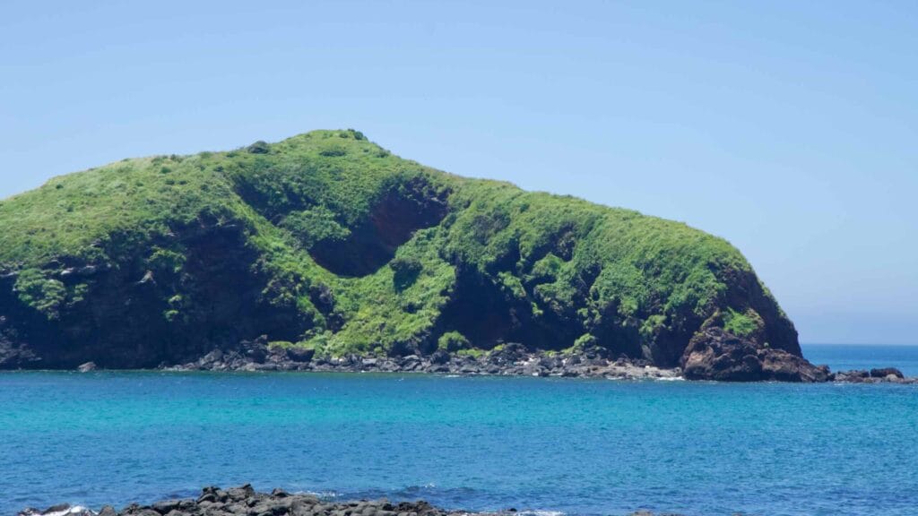 Green volcanic islet off Chagwido with red tuff scar and turquoise sea.