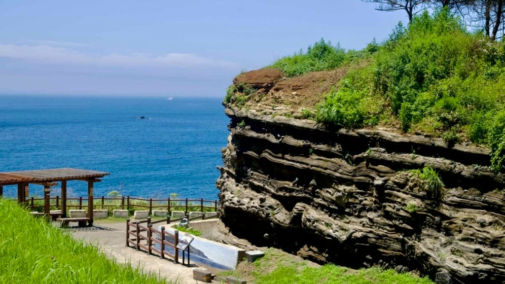 Layered tuff cliffs at Eongal coast beside a seaside walkway.