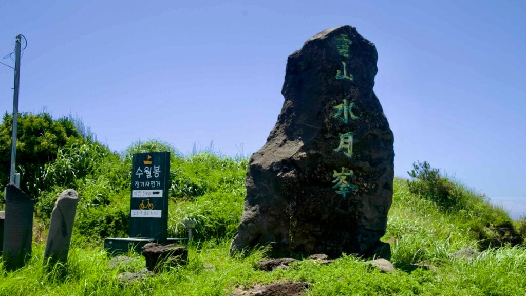 Suwolbong stone marker beside cycling signs on the grassy ridge.