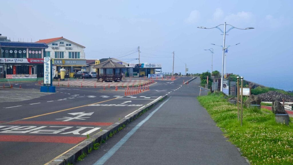 Hyeongjehaean‑ro curves past cafés and convenience stores with ocean views at Sagye.