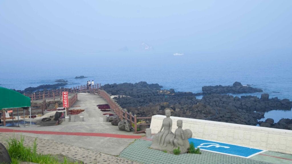 Jetty and tidal pools on Brother’s Coast Road with stone figures and distant islets.