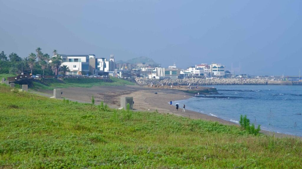 Sagye Beach curves toward the harbor and breakwaters under hazy light.