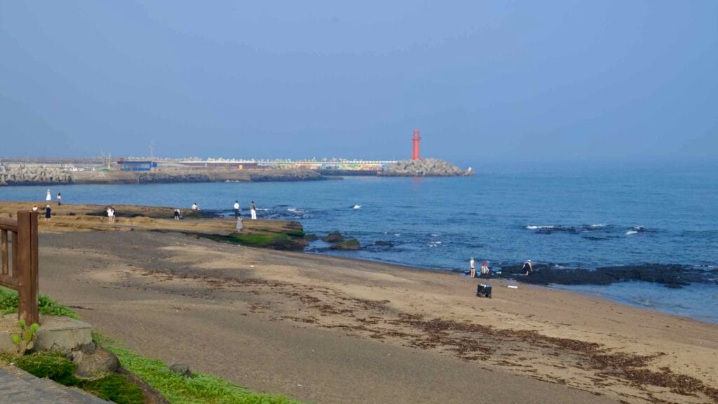 Sagye Beach with flat rock platforms and a red lighthouse on the breakwater.