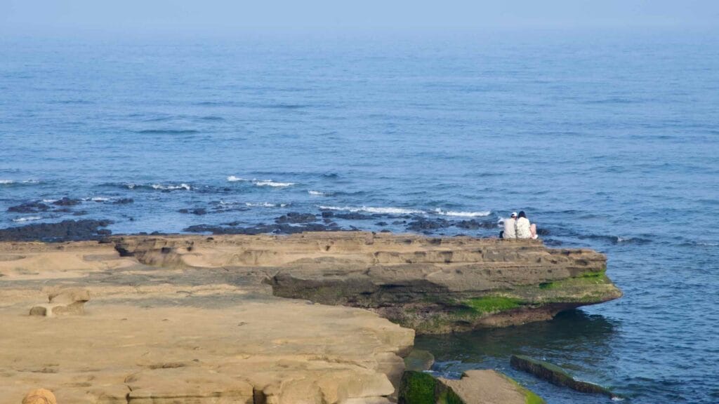 A couple sits on a tuff ledge above clear water at Sagye.