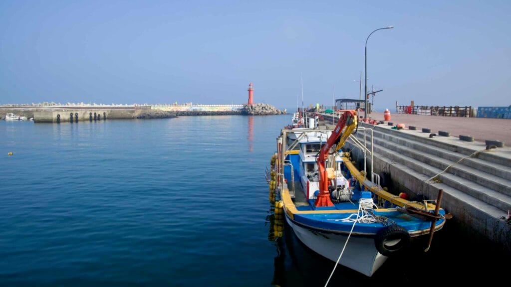 Fishing boat moored inside Sagye Port with red lighthouse beyond.