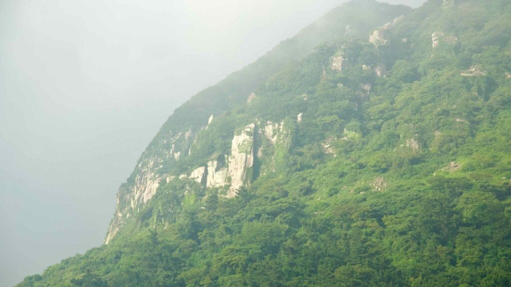 Sanbangsan’s wooded shoulder and pale rock outcrops fade into mist.