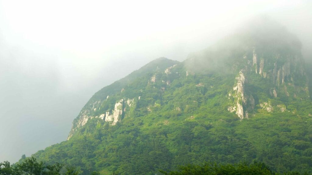 Clouds drape Sanbangsan as sun breaks across forested slopes.