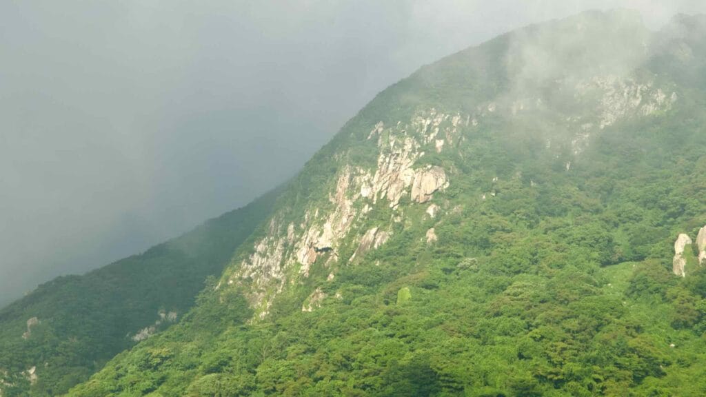 Haze drifts over Sanbangsan’s pale cliffs and evergreen slopes.