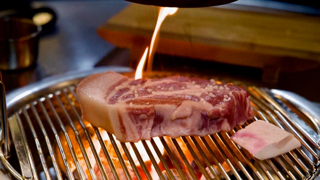 A flare kisses Jeju black pork on the charcoal grill.