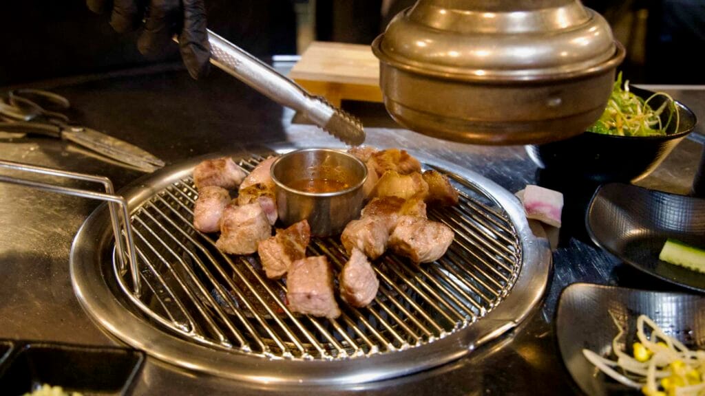 Cubes of Jeju black pork finish around a dipping cup.