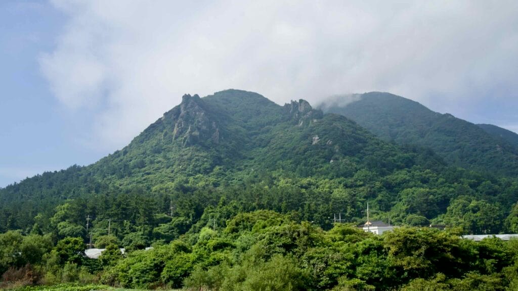 Twin ridges of Sanbang Mountain rise behind village trees, their rocky spires catching brief evening light.