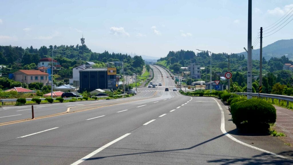 A long view along Iljuseo Road shows the divided highway passing houses and small businesses.