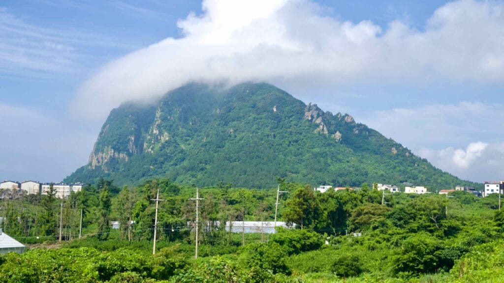 Sanbang Mountain spreads across the skyline with a cap cloud and rocky spurs above village fields.