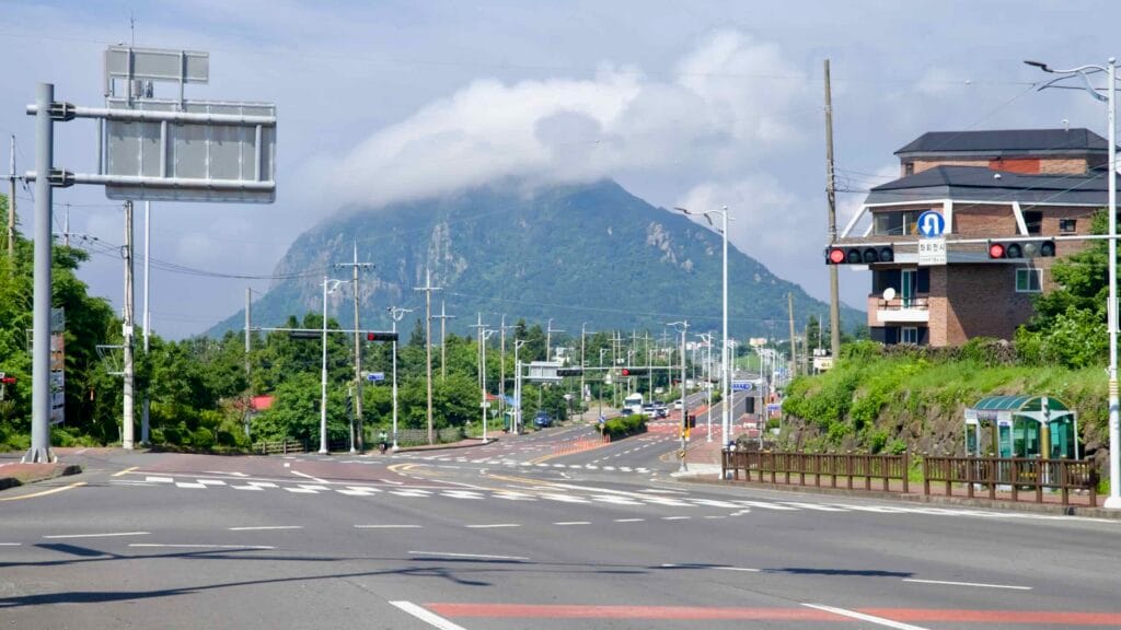 Traffic signals and lamp poles frame a distant view of Sanbang Mountain under a cap cloud.
