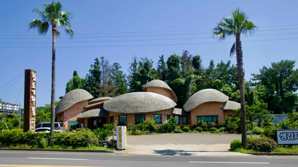 A roadside restaurant with dome-shaped roofs sits under palm trees and power lines in Jungmun.