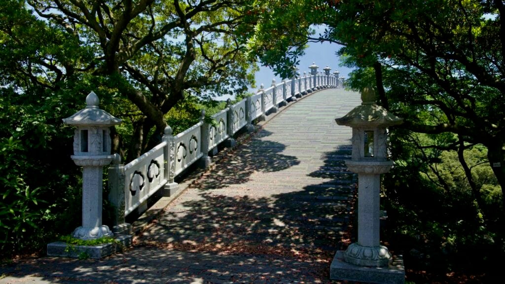 Shaded approach to Seonim‑gyo, the arched pedestrian bridge at Cheonjeyeon.
