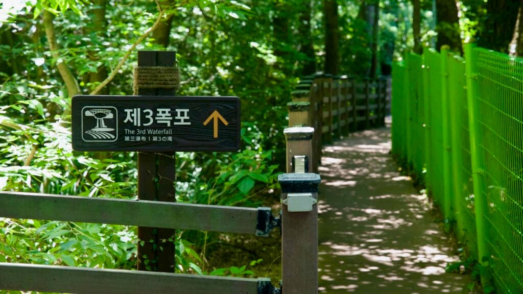 Bilingual sign on a shaded path points to Cheonjeyeon’s 3rd Waterfall.