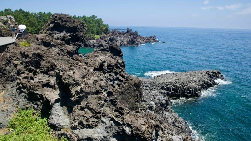 Waves break against basalt outcrops at the Jusangjeolli coastal cliffs.