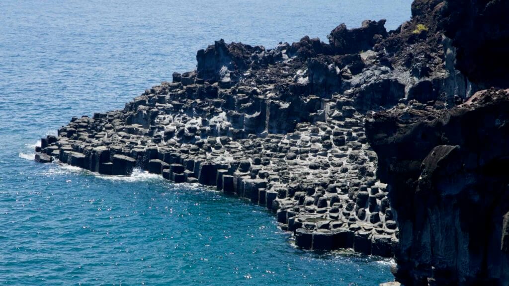 Stepped basalt shelves rise beneath a dark volcanic wall at Jusangjeolli.