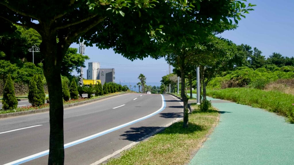 Ee-eo-do Road in Seogwipo has a bike path shaded by trees and a distant ocean view.