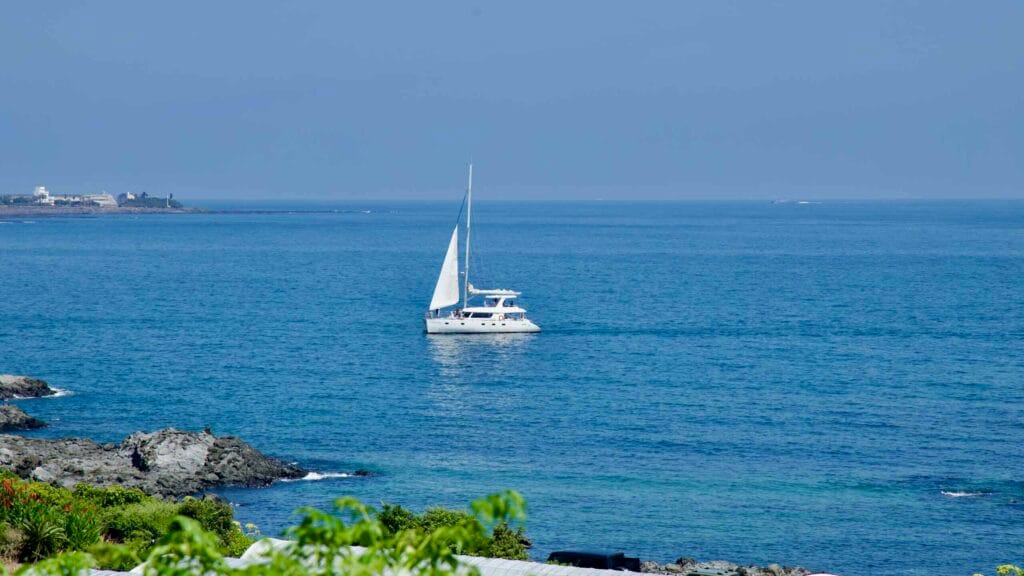A catamaran sails along the coast of Seogwipo with a lighthouse in the distance.