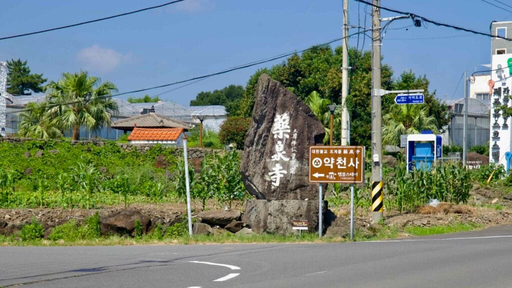 A stone marker and sign point to the entrance of Yakcheonsa Temple in Seogwipo.