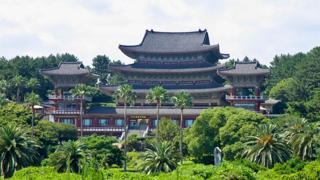 Yakcheonsa Temple’s tiered halls rise above palms and forest on a hillside near Seogwipo.