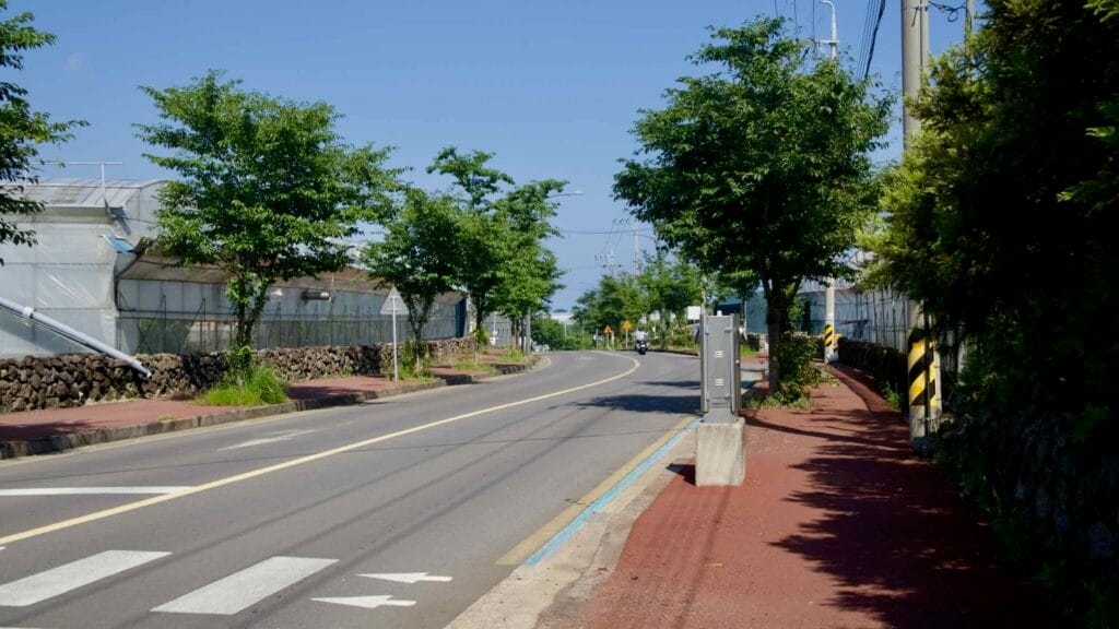 A rural road lined with greenhouses and basalt walls winds through farms near Seogwipo.
