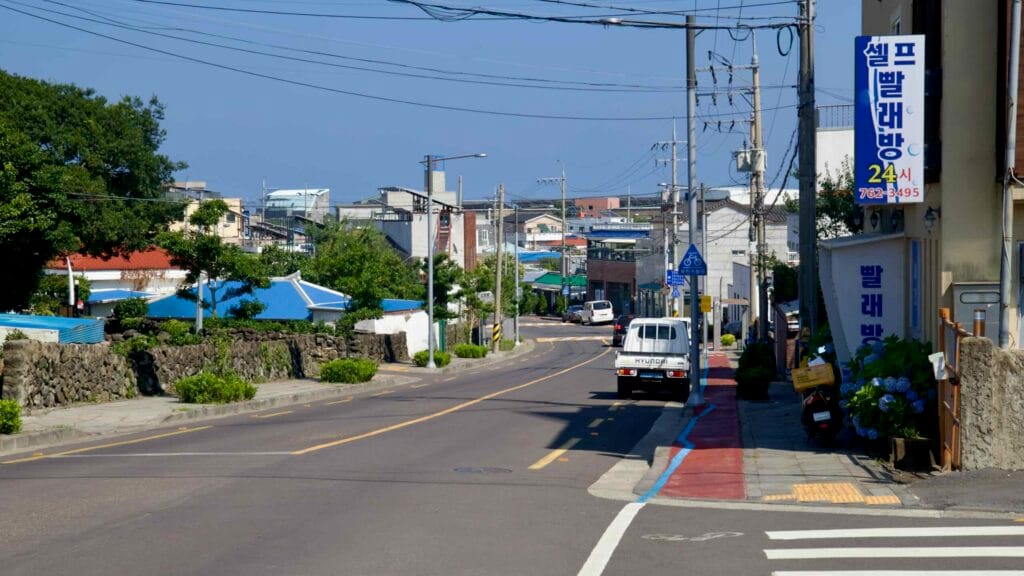 A neighborhood street lined with stone walls and shops descends toward the coast.