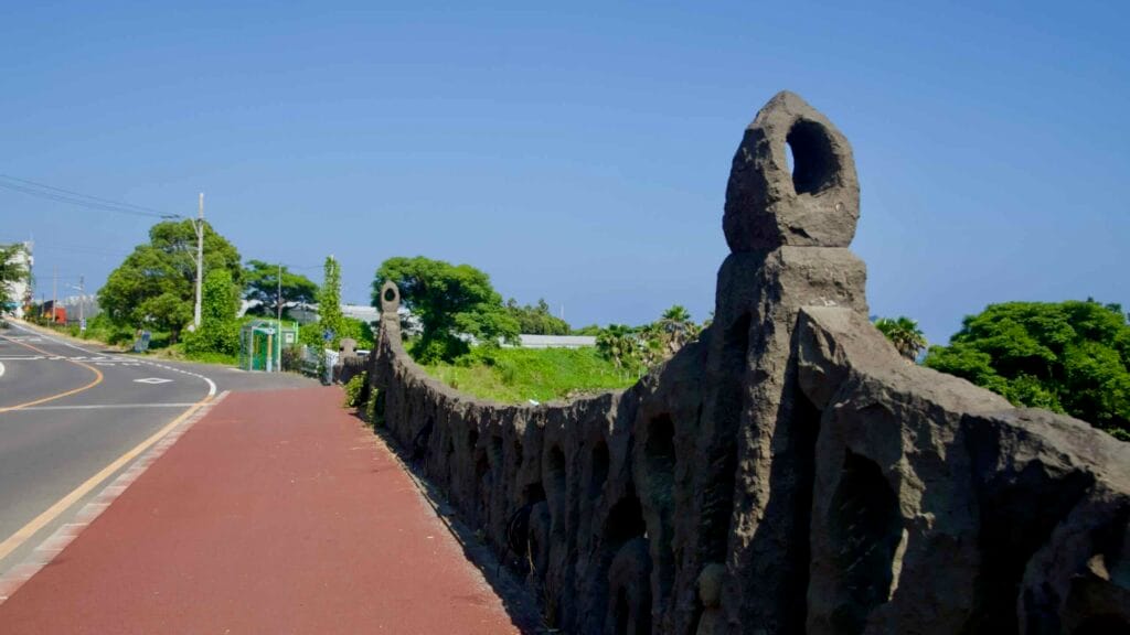 A basalt‑style balustrade lines a red walking path beside a curving road.