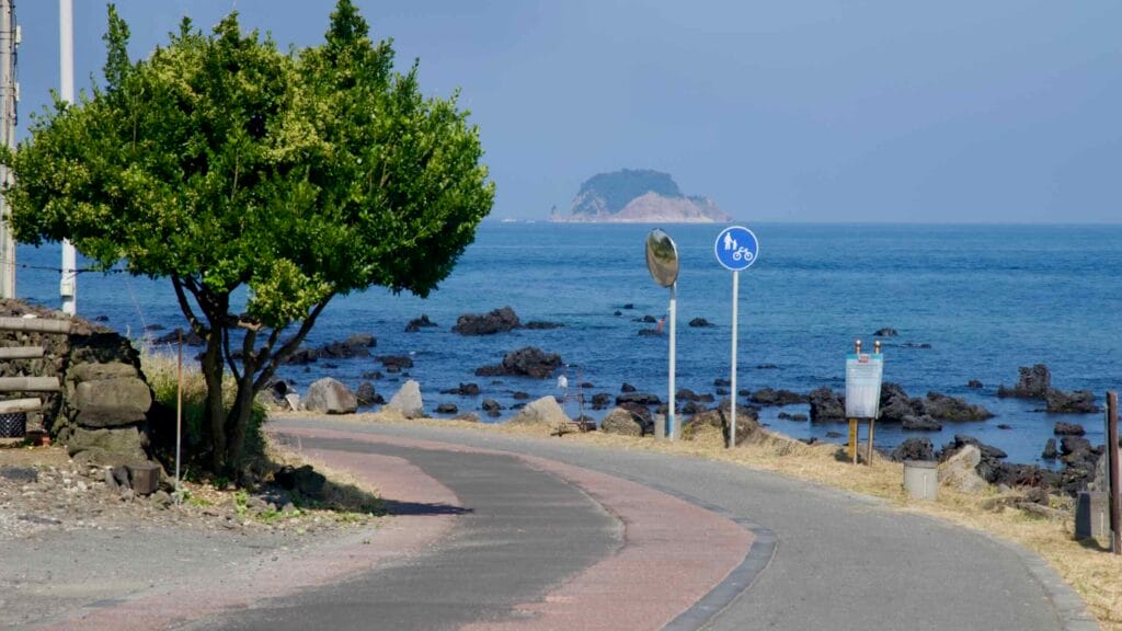 A shared bike and walking path follows the rocky coast with an islet offshore.