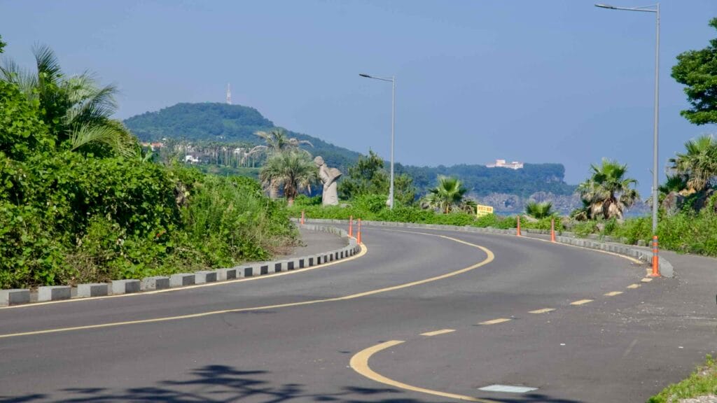 A palm-lined curved road near Beophwan with a haenyeo statue.