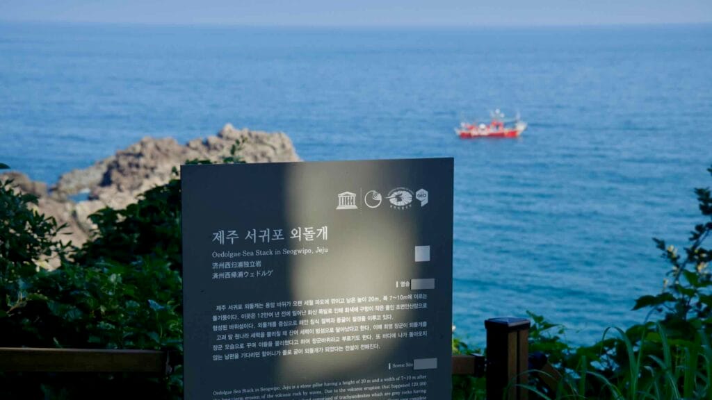 An informational sign about Oedolgae Rock overlooks the sea with a fishing boat in view.