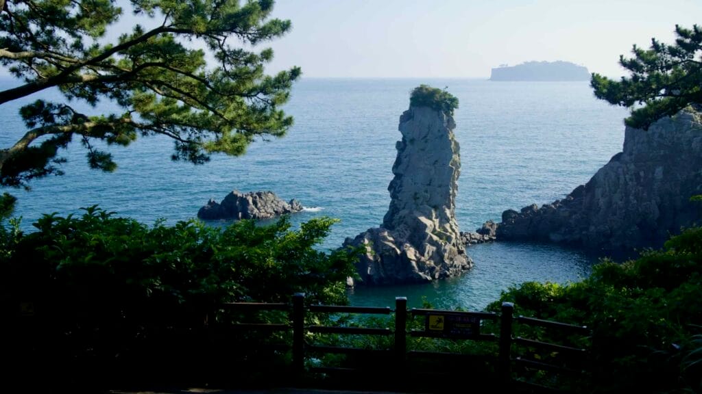 Oedolgae Rock stands tall beyond the trees along the coastal viewpoint.