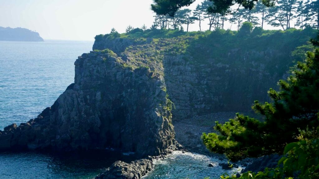 Basalt cliffs and pines frame a small cove near Oedolgae.